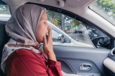 Endonezyalı bir müslüman kadın arabada beklerken uykulu ve esniyor.