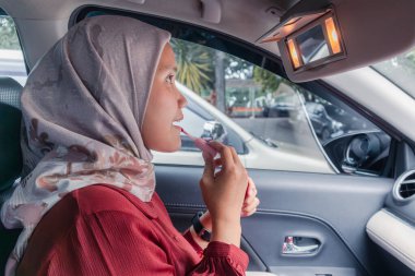 Endonezyalı Müslüman bir kadın arabada dudaklarına ruj sürüyor.