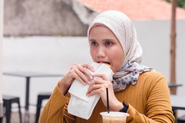 Endonezyalı Müslüman bir kadın dışarıda kahvaltı yapıyor.