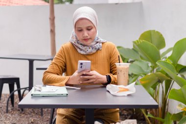 Endonezyalı Müslüman bir kadın kahvaltısını dışarıda yaparken akıllı telefonuyla mesajlara cevap veriyor.