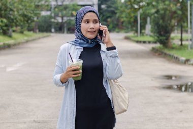 Genç Endonezyalı Müslüman bir kadın içkisini taşırken telefonla konuşuyor.