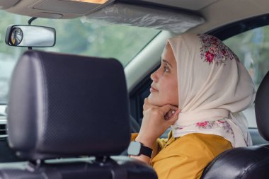 Genç Endonezyalı Müslüman bir kadın araba kullanmadan önce başörtüsünü düzeltirken aynaya bakıyor.