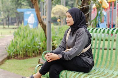 Parktaki bankta oturan Endonezyalı genç bir Müslüman kadın.