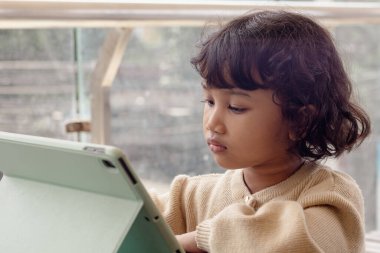 Küçük bir Endonezyalı Asyalı kız oyun oynamak için tabletine odaklanmış.