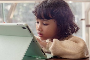 Küçük bir Endonezyalı kız oyun oynamak için tablet kullanıyor.