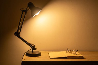 Sıcak ışıkta masanın üzerinde bir kitap ve gözlük.