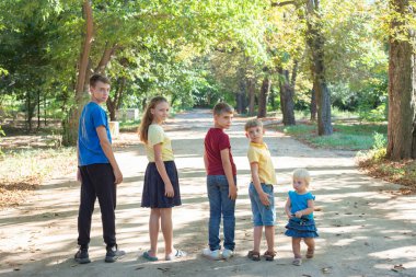 Beş çocuk parkta sıralanmış, doğada yürüyor ve dinleniyor..