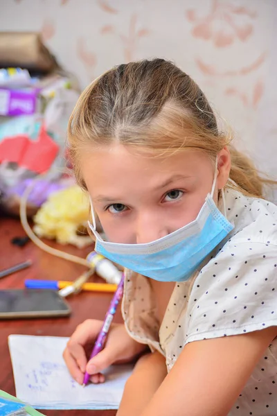 一名戴防护面具的女孩在家里做作业 在流感大流行期间进行隔离 — 图库照片