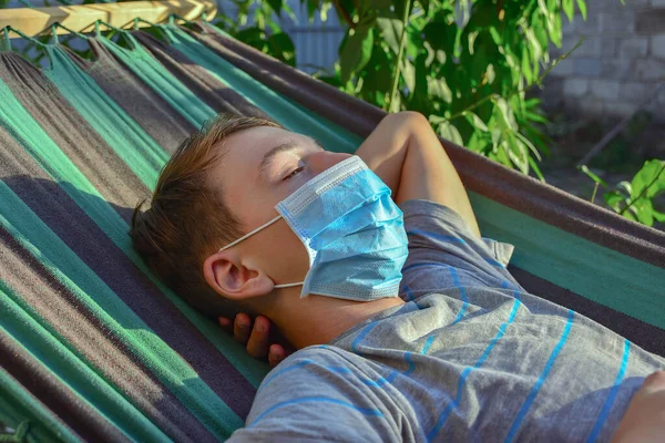 一名十几岁的男孩戴着防护面具躺在吊床上 这是在北欧大流行期间被隔离的 — 图库照片