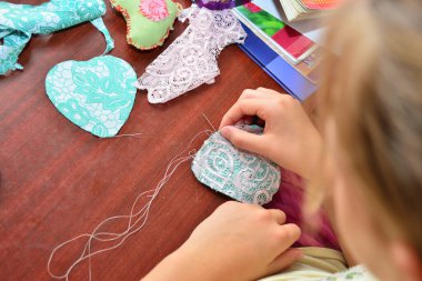 Bir kız kumaştan kalp diker, bir genç kız dikiş ve dikiş diker.