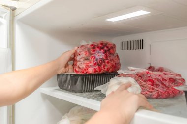 The woman takes out a bag of frozen cherries from the freezer. clipart