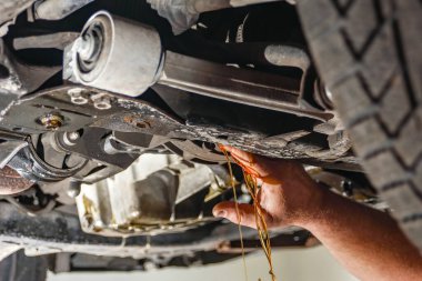 Çalışan bir araba tamircisi motor yağının boşaltılması ve yenilenmesi için krank kutusunun akış tıpasını açar..