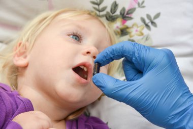 Mavi eldivenli bir doktor çocuğa kapsül ve tablet şeklinde ilaç verir..