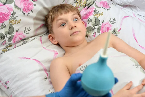 一个惊慌失措的孩子看到医生手里拿着一个医用灌肠器 — 图库照片