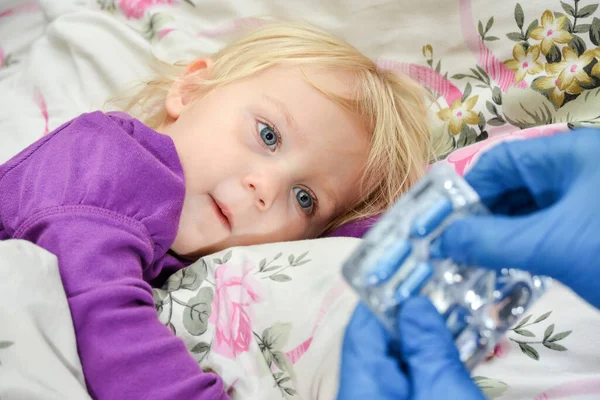 一个戴蓝色手套的医生给生病的孩子一粒药丸 — 图库照片