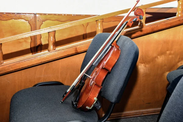 A violin with a bow and notes stands on a chair in the middle of an empty concert hall.
