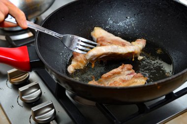 Kadın, kızarmış et parçalarını çatalla kızartma tavasında çeviriyor..
