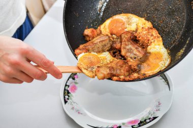 Bir kadın kızartma tavasındaki yumurtalarla kızarmış et koyar..