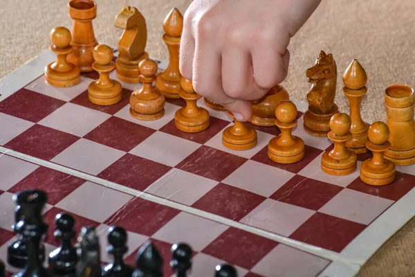 The player holds a white pawn in his hand and starts the game of chess.