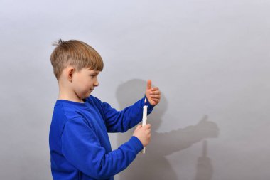 Çocuk yana doğru duruyor ve yanan bir mum tutuyor, sönmesin diye kapatıyor..