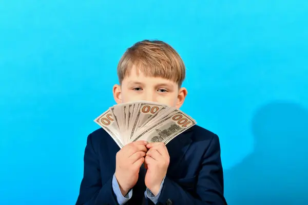 A boy in a suit holds money in a fan in front of him.