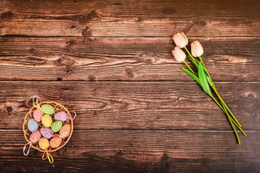 Paskalya yumurtaları ve laleler kahverengi ahşap bir dokuda yatar. Reklamlar ve metinler için yer.