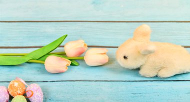 Sarı arka planda mavi bir ağaçtaki lalelerin yanında paskalya tavşanı. Yazıtlar, reklamlar ve metin için yer.