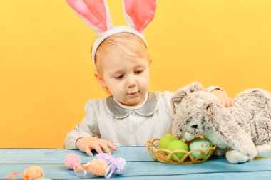 Küçük kız tavşanın yanında paskalya yumurtası sepeti tutuyor..