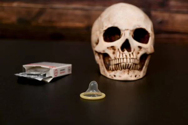 Opened condom near the skull on a dark background. Pregnancy, abortion and death concept.
