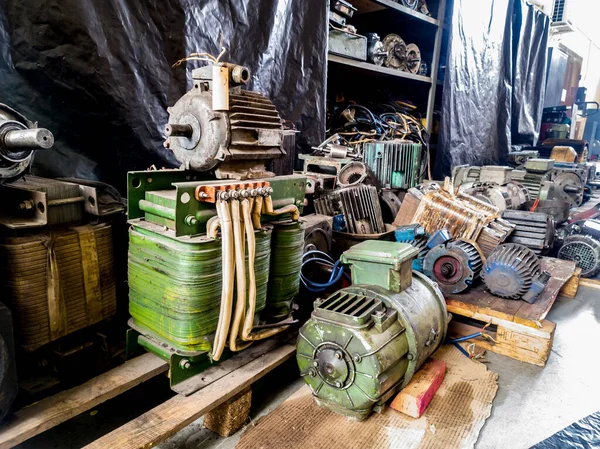 Warehouse of old non-working electric motors on racks and on the floor.