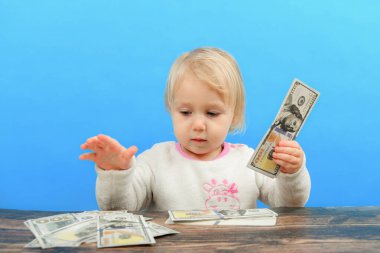 Küçük bir çocuk masanın üzerinde dolarları düzenliyor ve dikkatle onlara bakıyor..