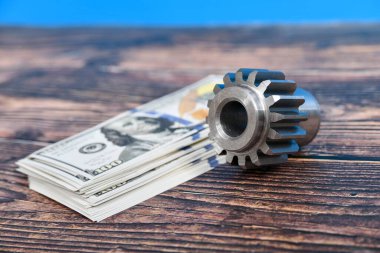 Vites kesme makinesinde yapılmış bir dişli tekerleği dolar banknotlarının üzerinde yatar. Reklam ve sanayi mühendisliği hizmetleri konsepti