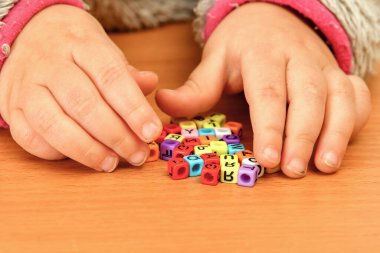 Küçük bir çocuk renkli harflerle oynar ve onları kelimelere dökmeye çalışır. Okul öncesi eğitim kavramı.