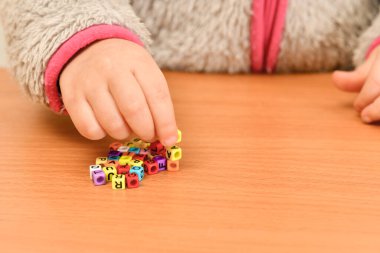 Küçük bir çocuk renkli harflerle oynar ve onları kelimelere dökmeye çalışır. Okul öncesi eğitim kavramı.