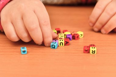 Küçük bir çocuk renkli harflerle oynar ve onları kelimelere dökmeye çalışır. Okul öncesi eğitim kavramı.