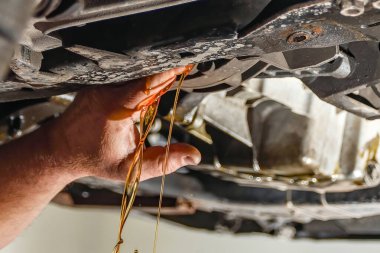 Çalışan bir araba tamircisi motor yağının boşaltılması ve yenilenmesi için krank kutusunun akış tıpasını açar..