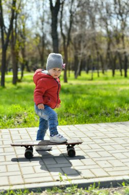Küçük çocuk kaykaya biniyor, çocuklar parkta yürüyor..