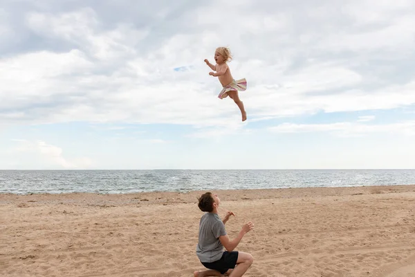 若いお父さんは彼の娘を投げ上げ 海岸で彼女をキャッチします — ストック写真