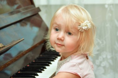 A little girl is sitting near the piano. Studying at a music school.