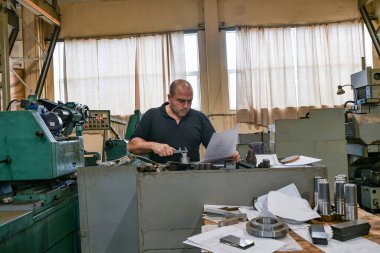 İşçi, vernier kalibre ile parçayı ölçer ve boyunu çizimle karşılaştırır..