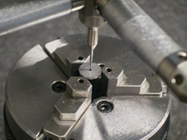 Yetenekli bir teknisyen, bir makine atölyesinde çevirmeli göstergeyle küçük metal bir parçayı ölçerek gün içinde üretimde kesinlik sağlıyor..