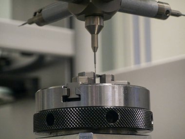 A high-precision measurement tool is positioned above a metal workpiece, ensuring accurate measurements in a busy manufacturing environment focused on quality assurance.