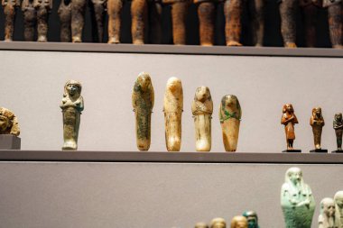 Küçük antik Mısır heykelcikleri bir müzenin raflarında sergilenir. Bu eserler çeşitli defin figürlerini tasvir ediyor ve eski bir medeniyetten eşsiz bir zanaat sergiliyor..