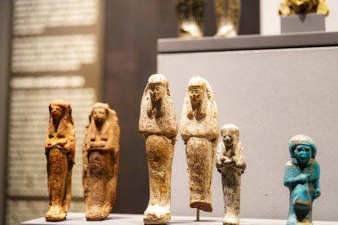 Renkli antik Mısır heykelleri bir müzede düzgünce düzenlenmiştir. Ziyaretçiler, geçmişteki figürleri tasvir eden bu eserlerin işçiliğine ve tarihsel önemine hayranlık duyuyorlar..