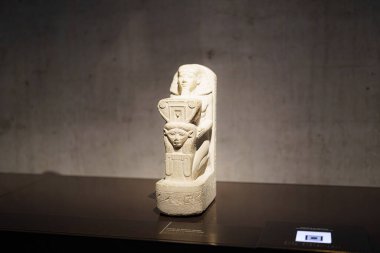 Bu antik Mısır kireç taşı heykeli, ayrıntılı oymalarla karakterize edilmiş, bir başlıkla süslenmiş bir figürü gösteriyor..