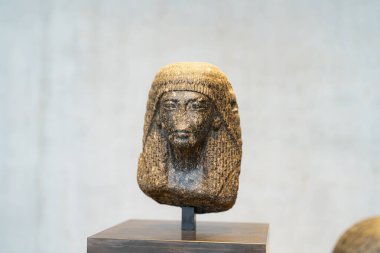 Antik Mısırlı bir kadını temsil eden detaylı bir heykel, çağdaş bir müzede belirgin bir şekilde sergilenmektedir. Eserde karmaşık şekilde oyulmuş özellikler ve gelenekler yer alıyor..
