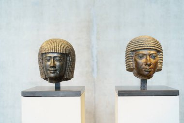 Antik Mısır 'dan iki detaylı heykel modern bir müzede sergilenmektedir. Taş kafalar, kültürün sanatsal başarılarını vurgulayan farklı saç şekilleri ve ifadeler sergiliyor..