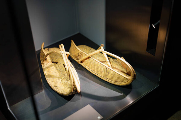 A pair of traditional woven sandals are showcased in a museum exhibit, highlighting craftsmanship and cultural heritage. The sandals rest in a glass display, inviting curiosity.