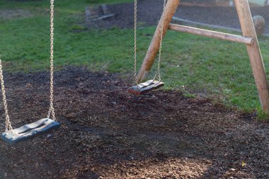 Parktaki ahşap bir çerçeveye nazikçe asılı iki boş salıncak. Güneş ışığı, sakin bir öğleden sonra, huzurlu ve davetkar bir sahne yaratıyor..