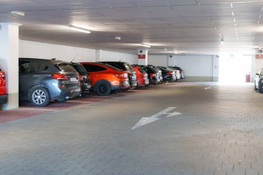 Farklı renkte arabalar, düzgün aydınlatılmış, kapalı bir otoparka park edilmiş. Ok izleri yol gösterici sürücüler. Parlak çıkış garajın diğer ucunda görünüyor..